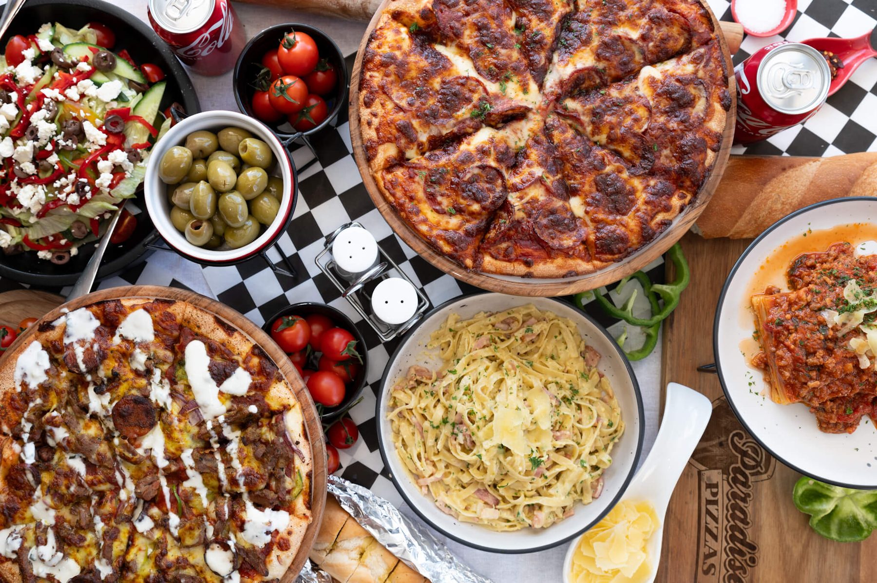 Paradise Pizzas table — pies, carbonara, lasagna and salad on the checkered runner